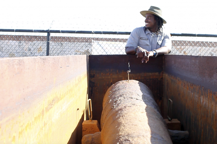 Maintenance Worker Norman Rutherford smiles next to a historic cannon at San Juan National Historic Site